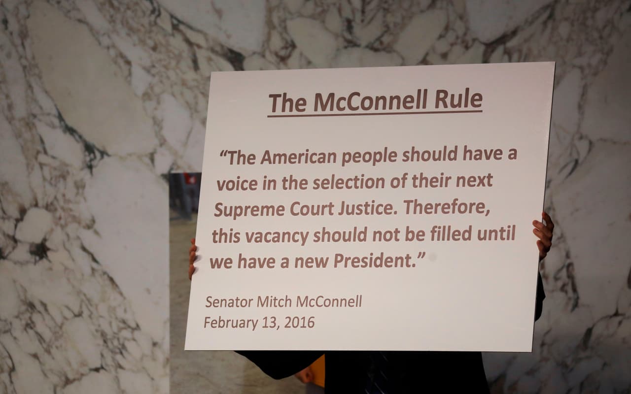 Un cartel con la ‘regla McConnell’ fue mostrado en la audiencia de la jueza Barret. Desde que murió la magistrada Ruth Bader Ginsburg, los demócratas han recordado a los republicanos cómo en 2016 el presidente Barack Obama no pudo llenar la vacante en la Corte Suprema que dejó la muerte de Antoin Scalia, con el argumento de que no podía hacerse en año electoral. 
<br>