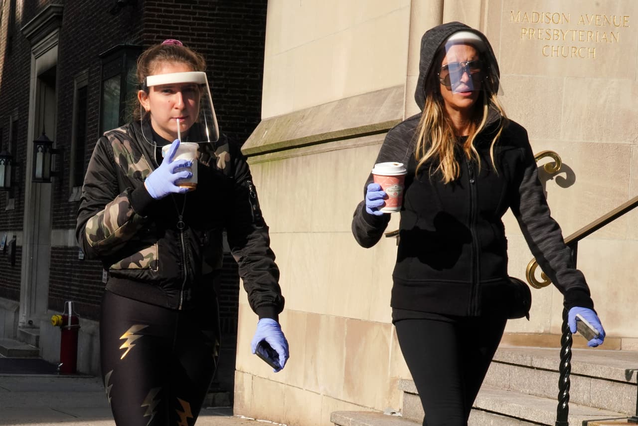 Mujeres salen por su café usando protectores de plastico para cubrirse la cara