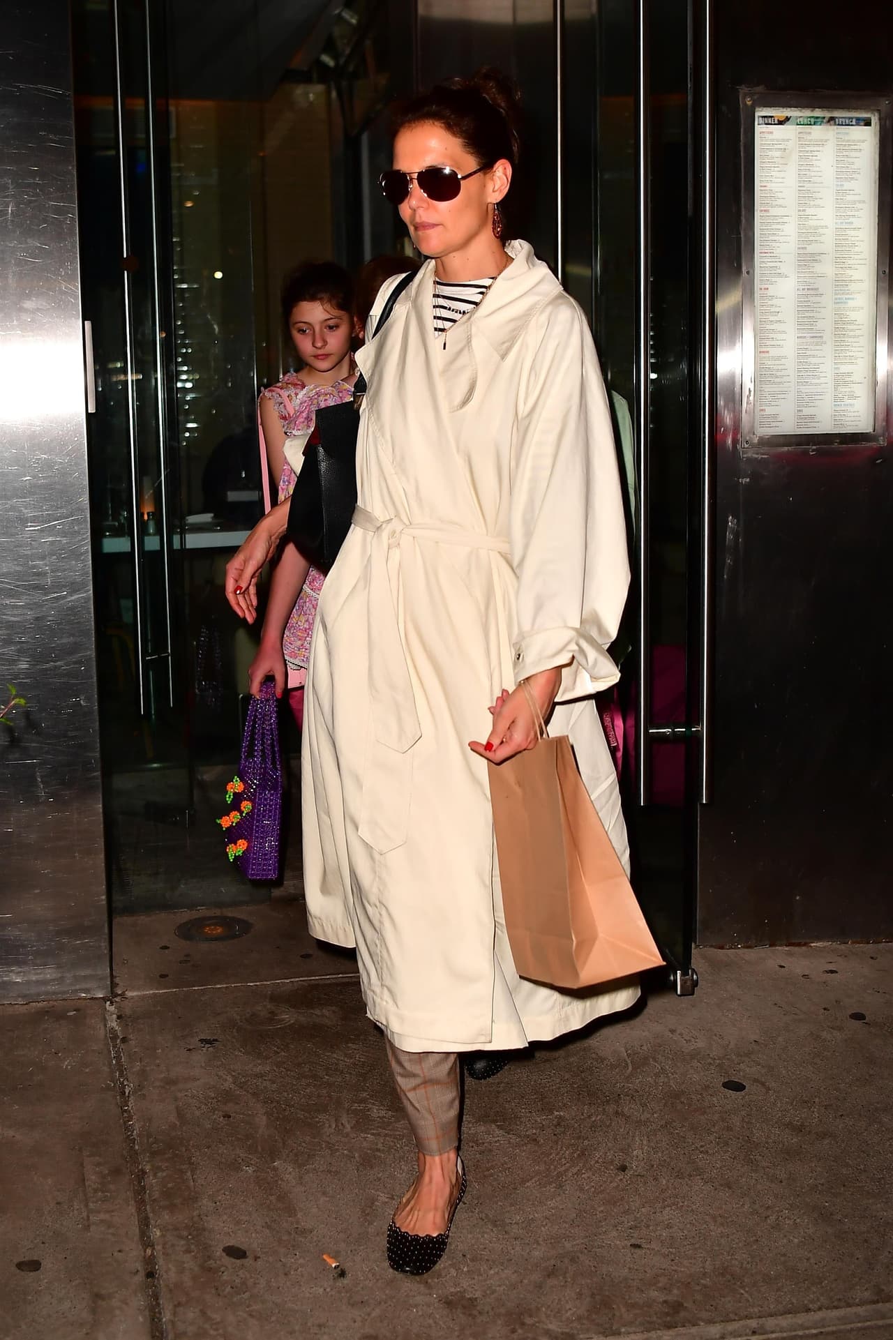 Katie Holmes vestía una gabardina blanca y debajo una blusa a rayas, pantalones capri y zapatos abiertos en tono oscuro.