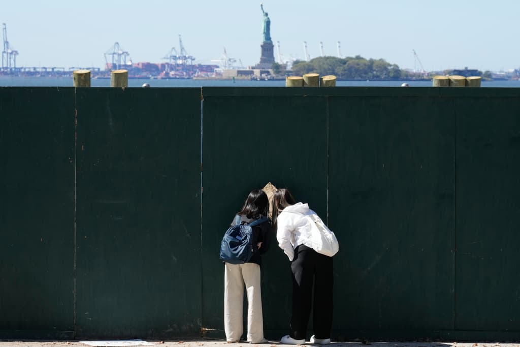 Personas observan a través de una abertura en una cerca para ver la Estatua de la Libertad en Nueva York, 
<a href="https://www.univision.com/local/washington-dc-wfdc/cierre-de-gobierno-en-ee-uu-retrasos-en-snap-alza-en-seguros-de-salud-y-un-mes-sin-pagos">durante el primer día del cierre de gobierno</a>, el 1 de octubre de 2025.