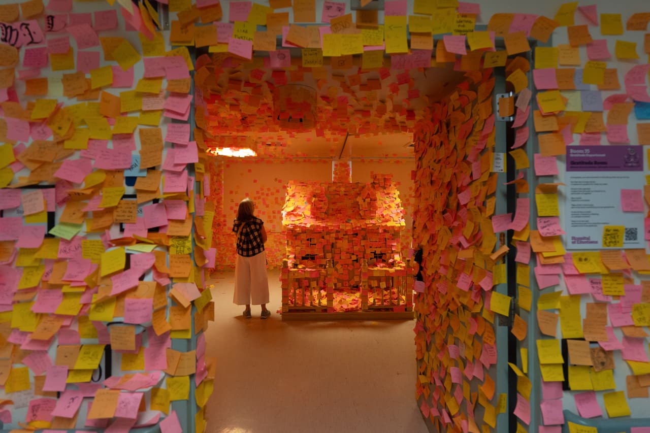 Un visitante se encuentra en la Sala de la Gratitud, cubierta de notas manuscritas, durante la exposición "Hospital de las Emociones" en un antiguo edificio hospitalario de Los Ángeles, el miércoles 22 de julio de 2026. (Foto AP/Jae C. Hong)
