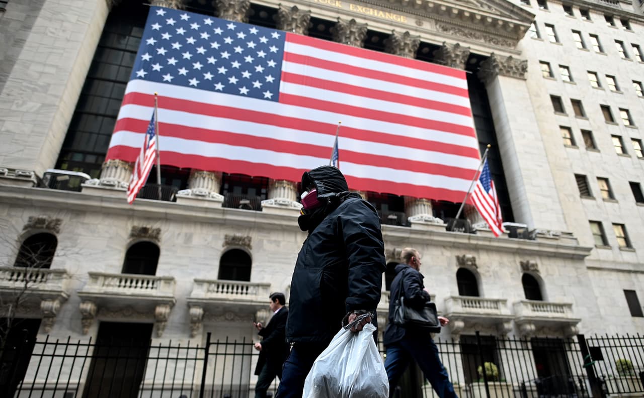 Un hombre con mascarilla pasa con su compra frente a la bolsa de Nueva York.