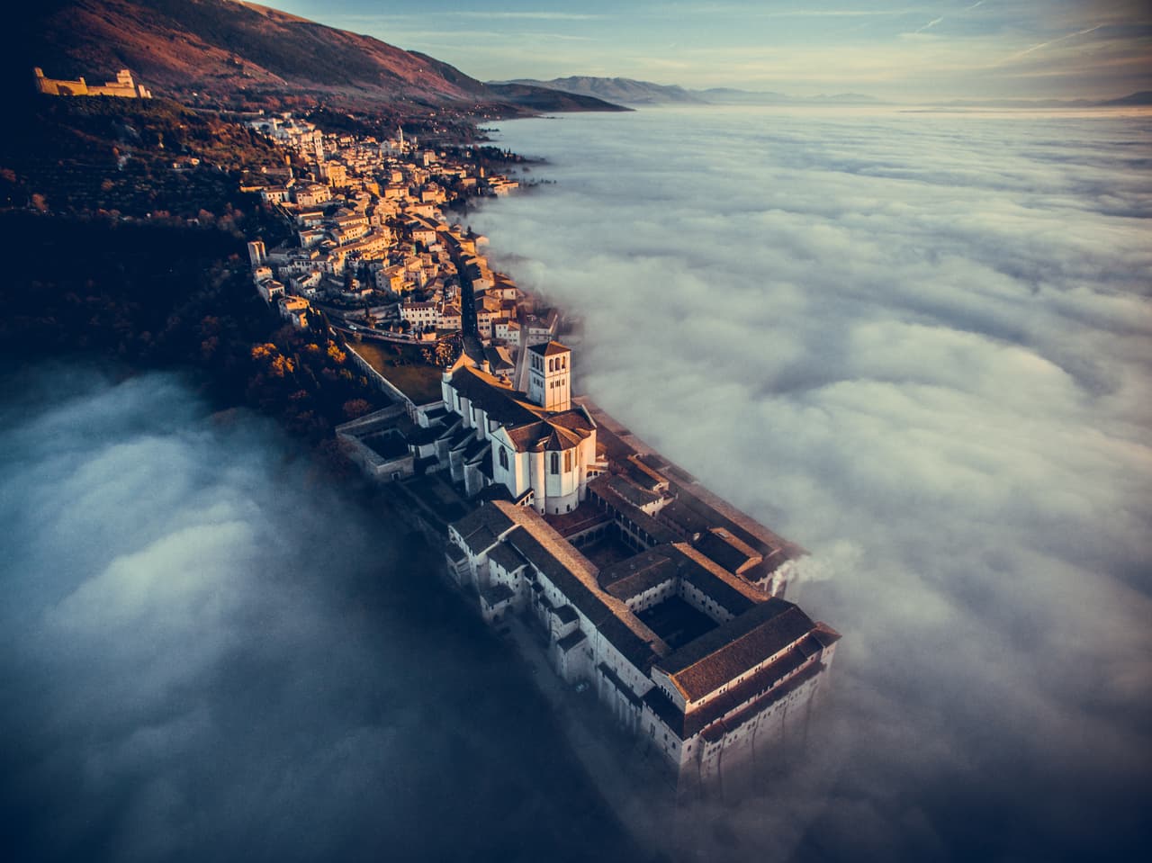 Las nubes abrazan la montaña y dejan al descubierto a la Basílica de San Francisco de Asís en Umbría, Italia.