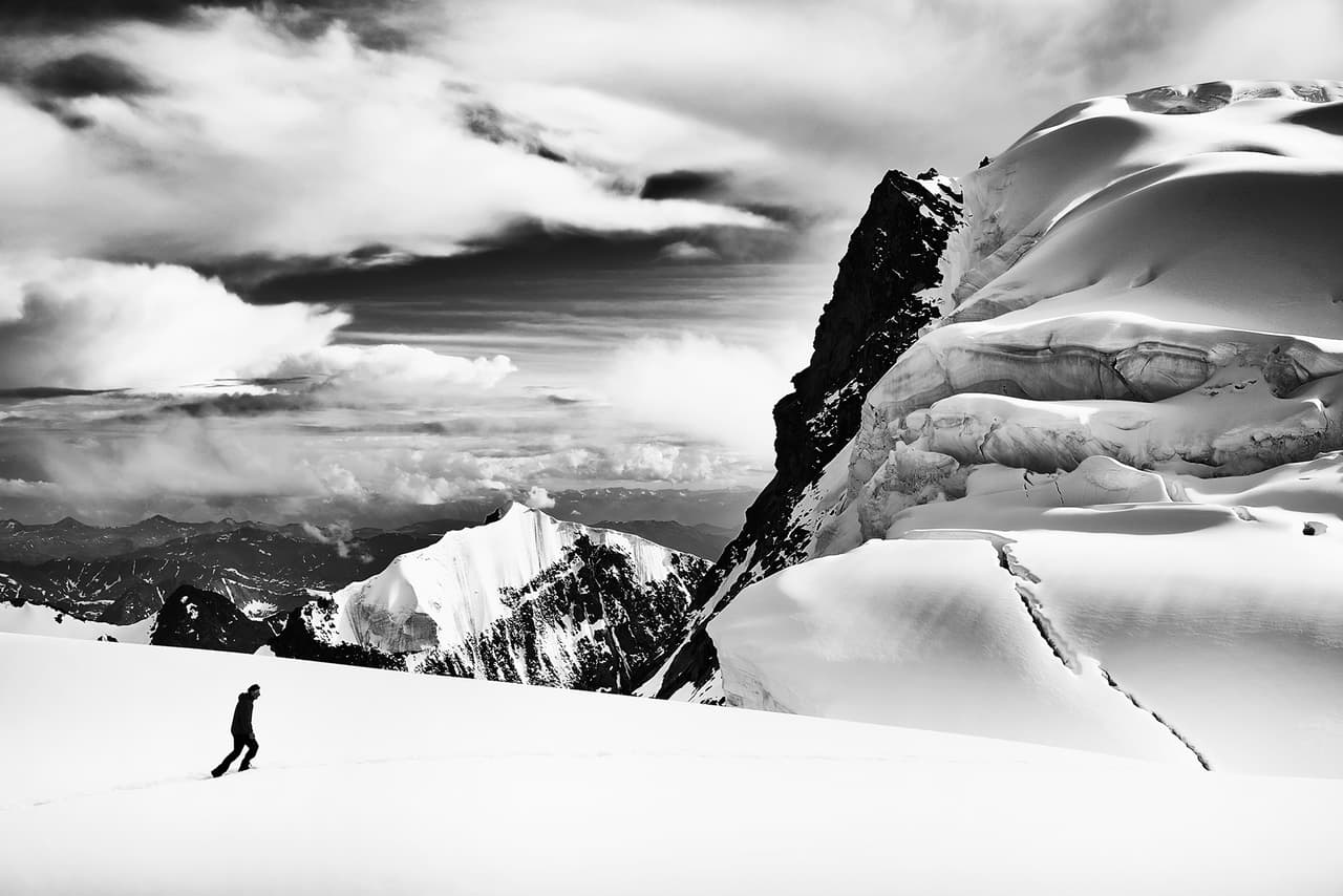Fotografía blanco y negro de un alpinista caminando cerca de la cima del monte Beluja. Esta es la cumbre más alta del macizo de Altái que se encuentra en la frontera entre Rusia y Kazajistán.