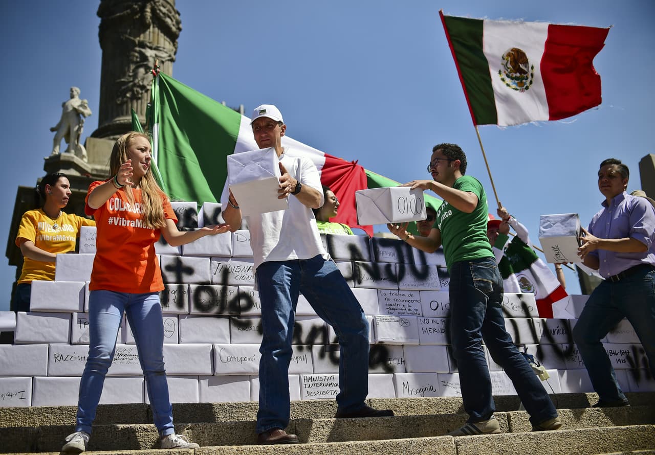 Un grupo de activistas cargan bloques que simulan ladrillos y construyen un muro ficticio a los pies del Ángel de la Independencia.