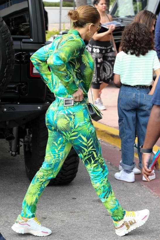 Esta vez el 'real jungle dress' de Donatella Versace volvió en un conjunto casual de pantalón y camisa que complementó con unos tenis blancos de agujetas doradas, lentes de sol verdes y aretes plus size dorados.