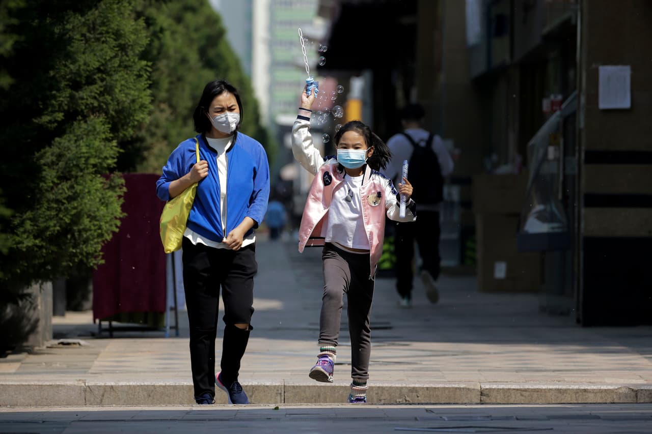 Un niño con una máscara facial protectora para ayudar a frenar la propagación del nuevo coronavirus juega con burbujas junto a una mujer, el martes 28 de abril de 2020.