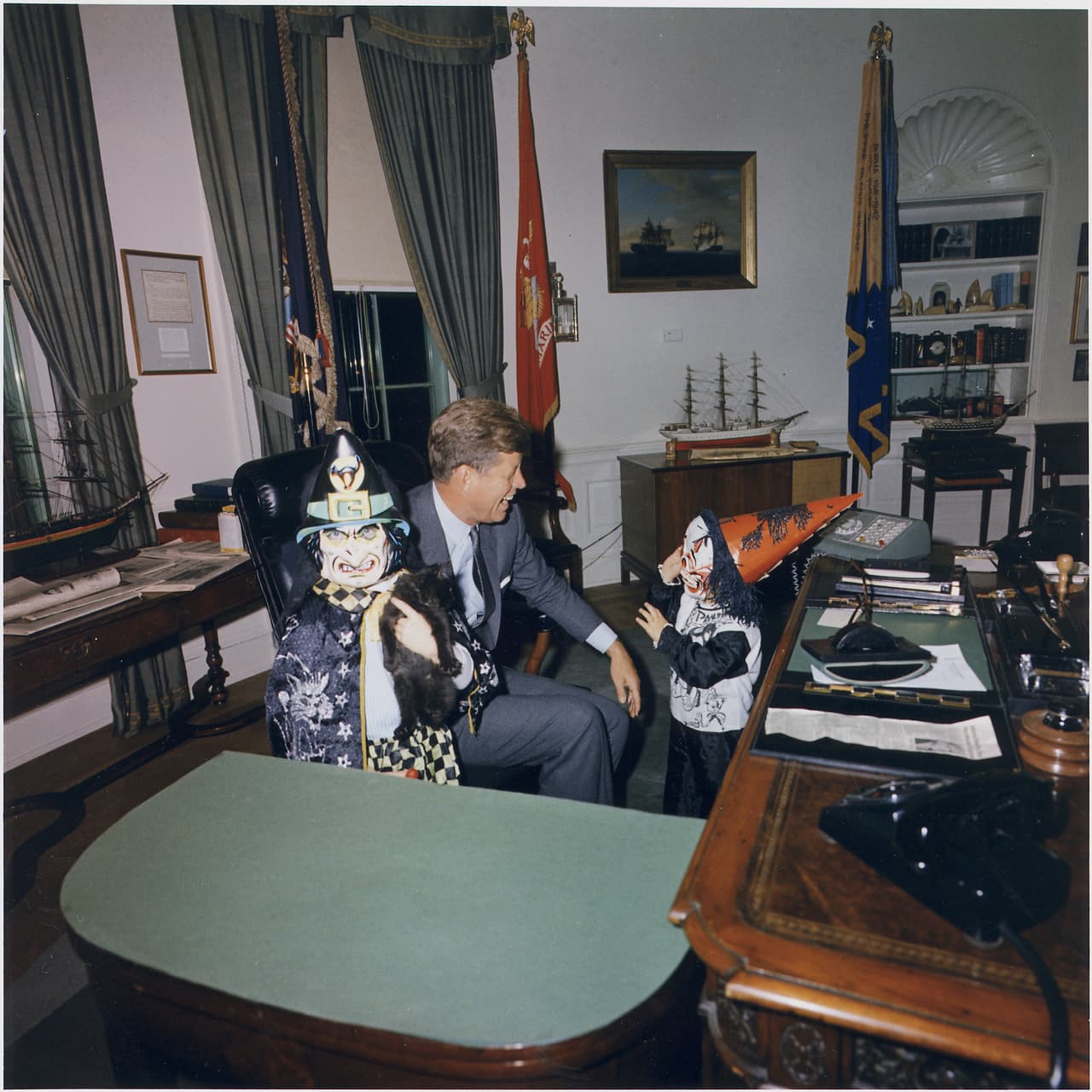 Unos espantosos personajes hacen reír a carcajadas al presidente John Fitzgerald Kennedy (1961-1963) en su despacho.
