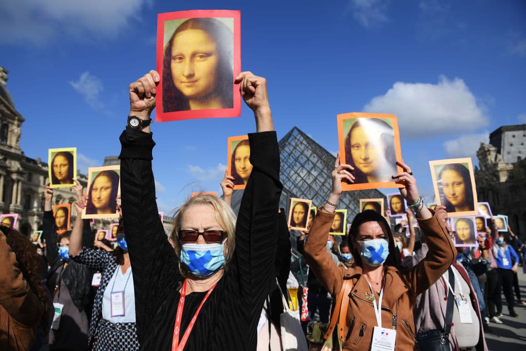 Guías turísticas sostienen retratos de la Mona Lisa frente al Louvre que reabre tras cuatro meses cerrado por la pandemia de coronavirus.
