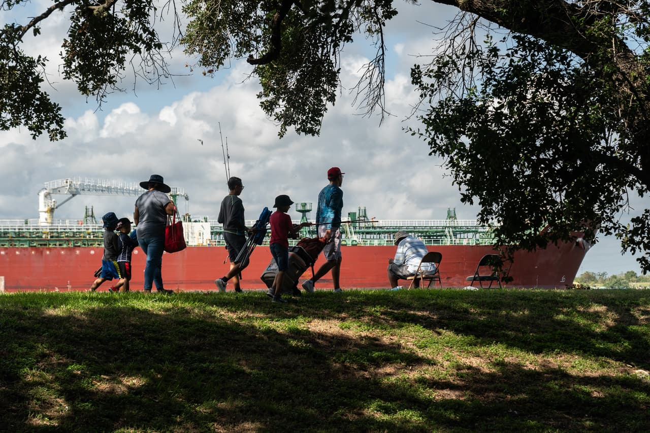 Un grupo de personas camina por el Parque San Jacinto mientras un barco cisterna pasa por el Canal de Navegación de Houston en La Porte. Miles de familias viven y juegan cerca del complejo petroquímico más grande del mundo.