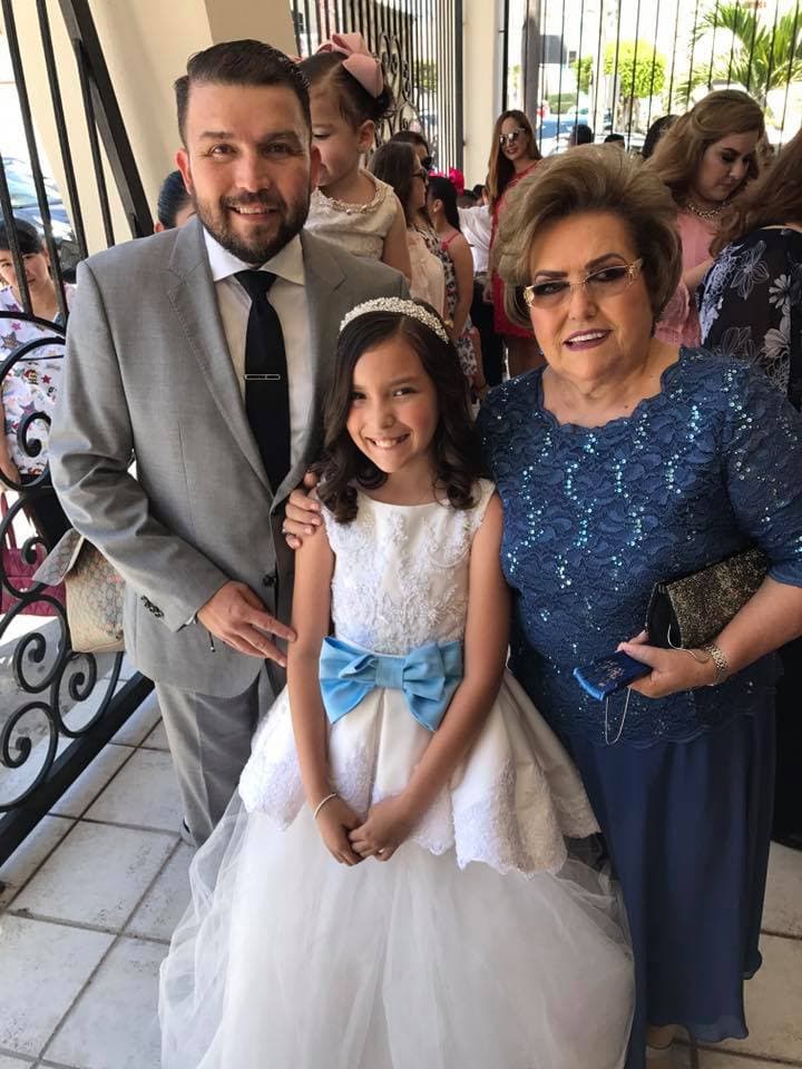 Doña Chuyita Lizárraga posó al lado de su hijo Poncho y de la festejada, quien portó un vestido blanco con aplicaciones y un moño azul cielo al frente.