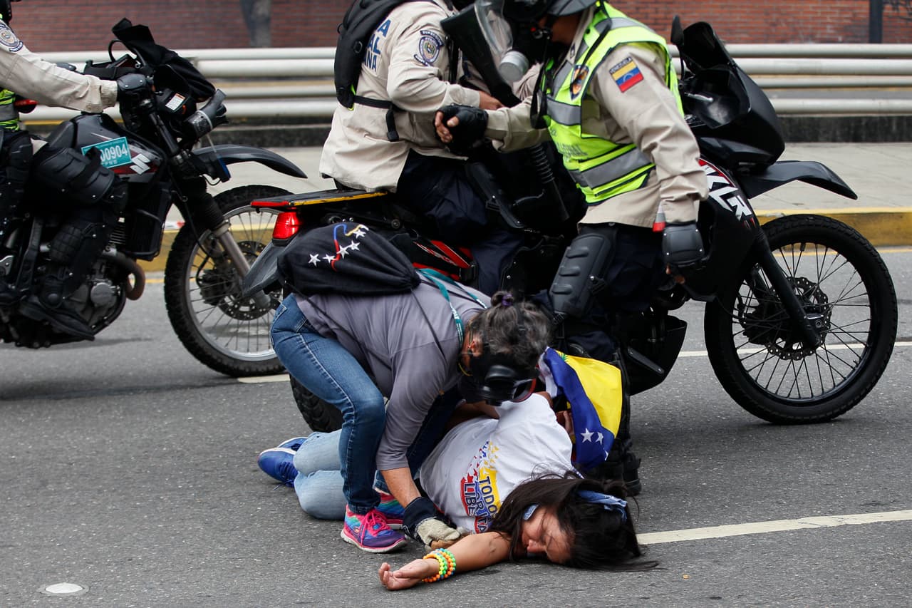 Una mujer desmayada durante una protesta contra Nicolás Maduro en 2017 es asistida por otra persona, que además la protege de un funcionario de la Policía Nacional.