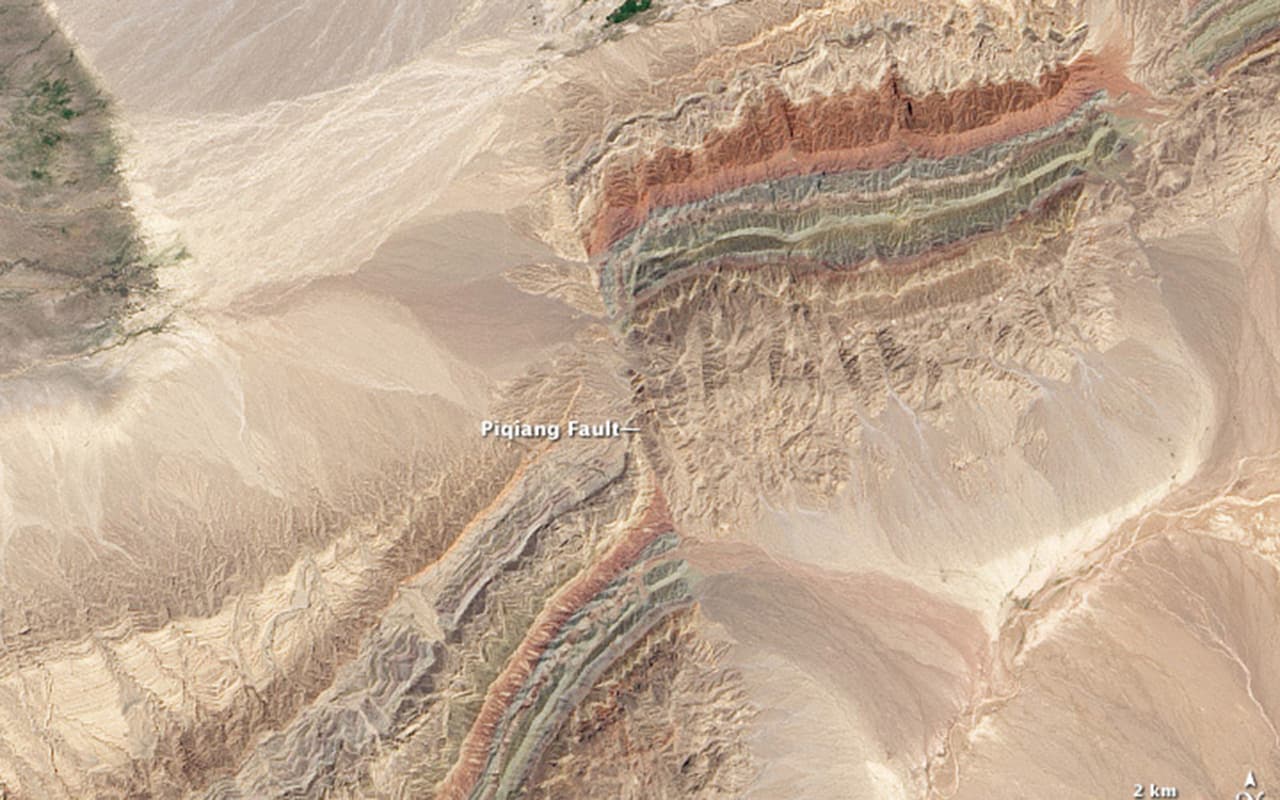 <b>Fallas en Xinjiang. </b>Justo al sur de las montañas de Tien Shan, en el noroeste de la provincia de Xinjiang, las colinas más altas se elevan hasta 3,900 pies (1,200 metros) y se ven capas de rocas sedimentarias de color rojo, verde y beige. Los colores reflejan rocas que se formaron en diferentes momentos y en diferentes entornos. Las capas rojas son areniscas formadas por antiguos ríos, las verdes son areniscas formadas en un océano de profundidad moderada, y las de color crema son calizas formadas en un océano poco profundo.
<br>