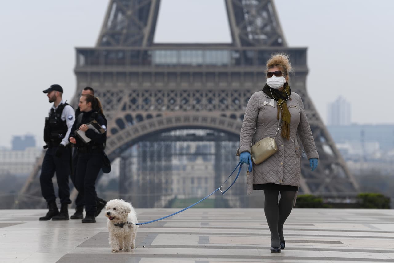 Una mujer pasea con su mascota al lado de la Torre Eiffel en Paris, mientras usa tapabocas y guantes para evitar el contagio de covid-19.
