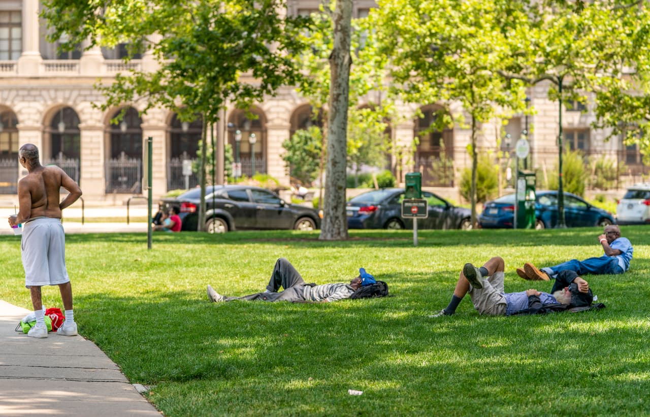 Ante la falta de aire acondicionado en sus casas, estos residentes buscan el cobijo de la sombra en un parque.