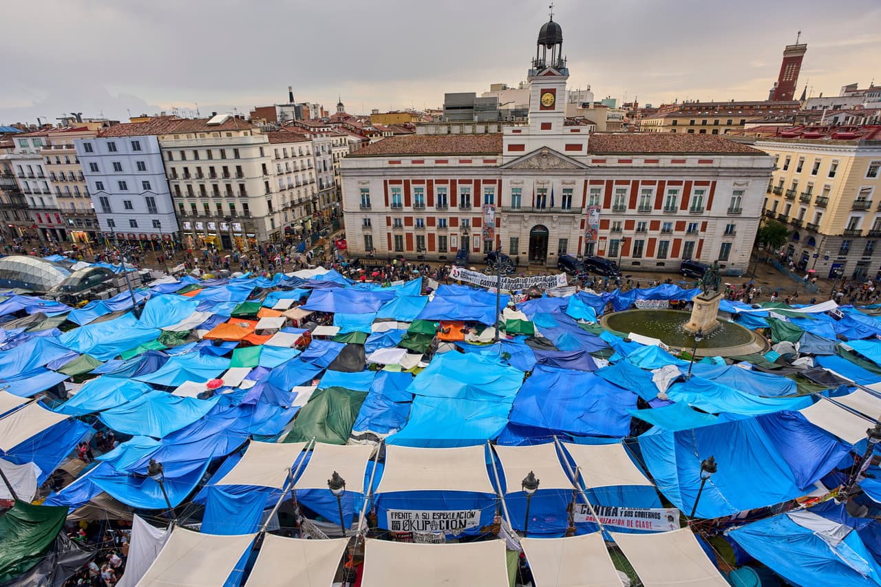 Unos activistas se resguardan de la fuerte lluvia mientras acampan en la Puerta del Sol —tras el desahucio de María del Carmen Abascal, de 87 años— para exigir leyes más estrictas que protejan a los inquilinos en Madrid, España, el viernes 2 de octubre de 2026.