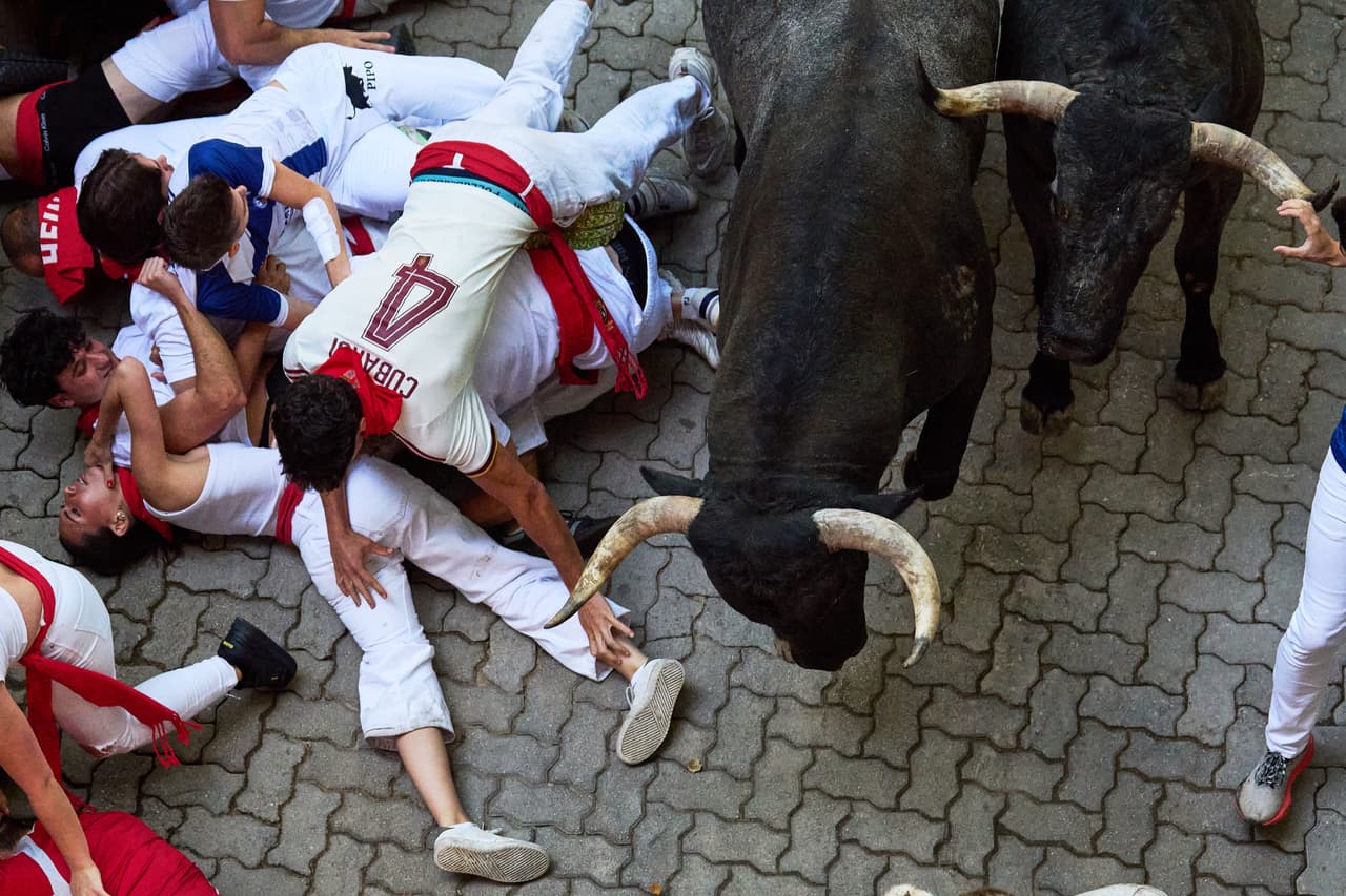 Participantes caen al suelo junto a los toros de lidia de José Escolar durante el quinto encierro de las fiestas de San Fermín
