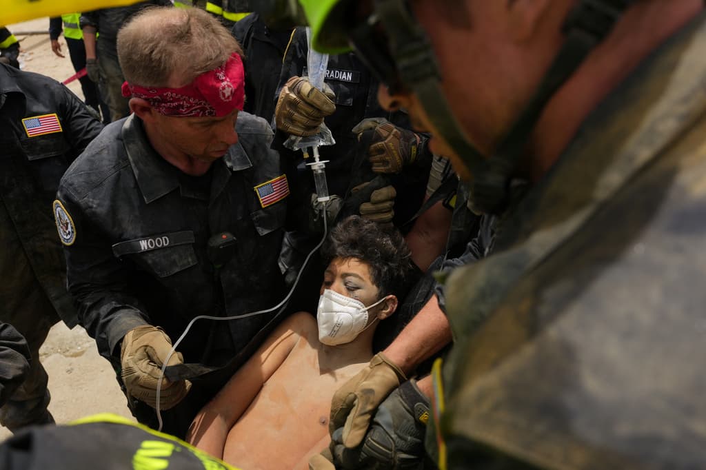 Bomberos estadounidenses del equipo de búsqueda y rescate del condado de Fairfax sacan a un niño de entre los escombros tras rescatarlo a él y a su padre de un edificio que colapsó durante los terremotos en La Guaira, Venezuela, el domingo 28 de junio de 2026. (Foto AP/Matias Delacroix)
