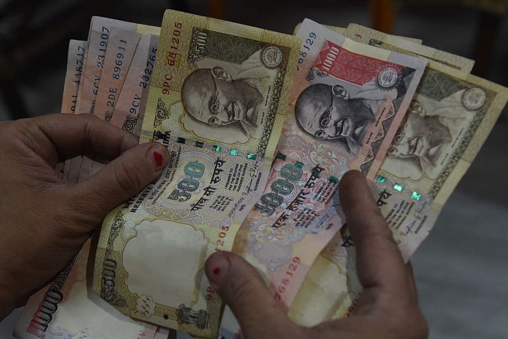 Mujer sosteniendo billetes con denominación de 500 y 1000 rupias indias.