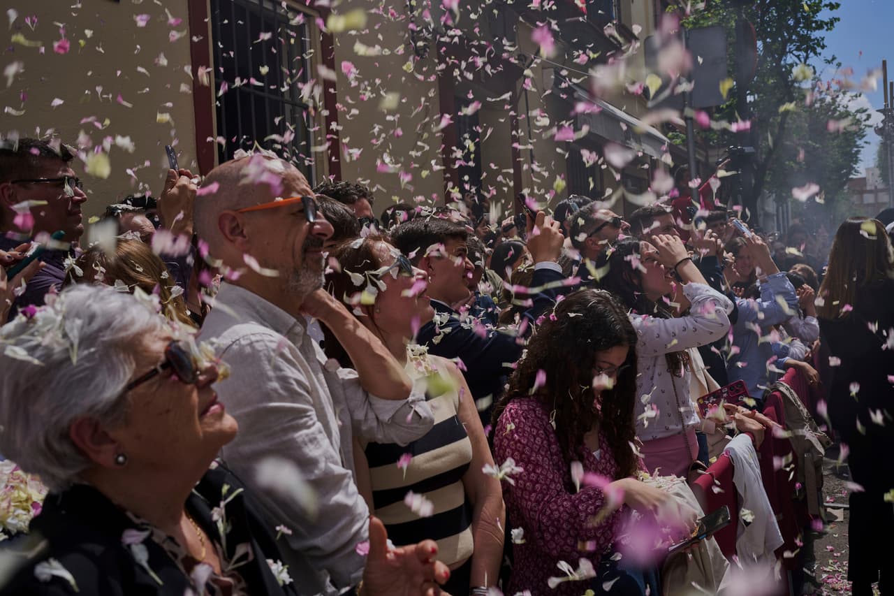 Personas son bañadas con pétalos de flores lanzados desde balcones durante una procesión de Semana Santa en Sevilla, España, el domingo 13 de abril de 2025.