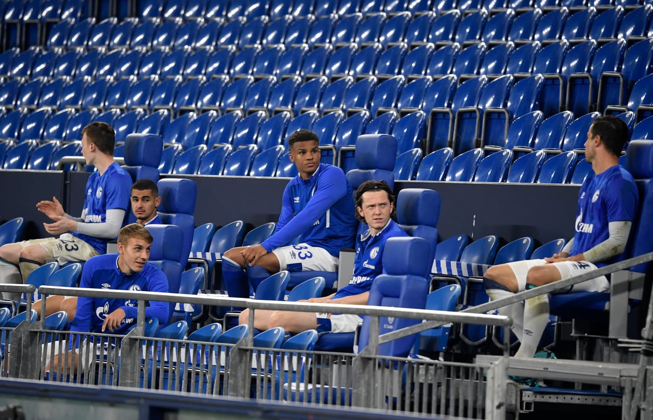 Los suplentes del Schalke 04 esperan en la banca con la distancia social recomendada mientras son requeridos para jugar.