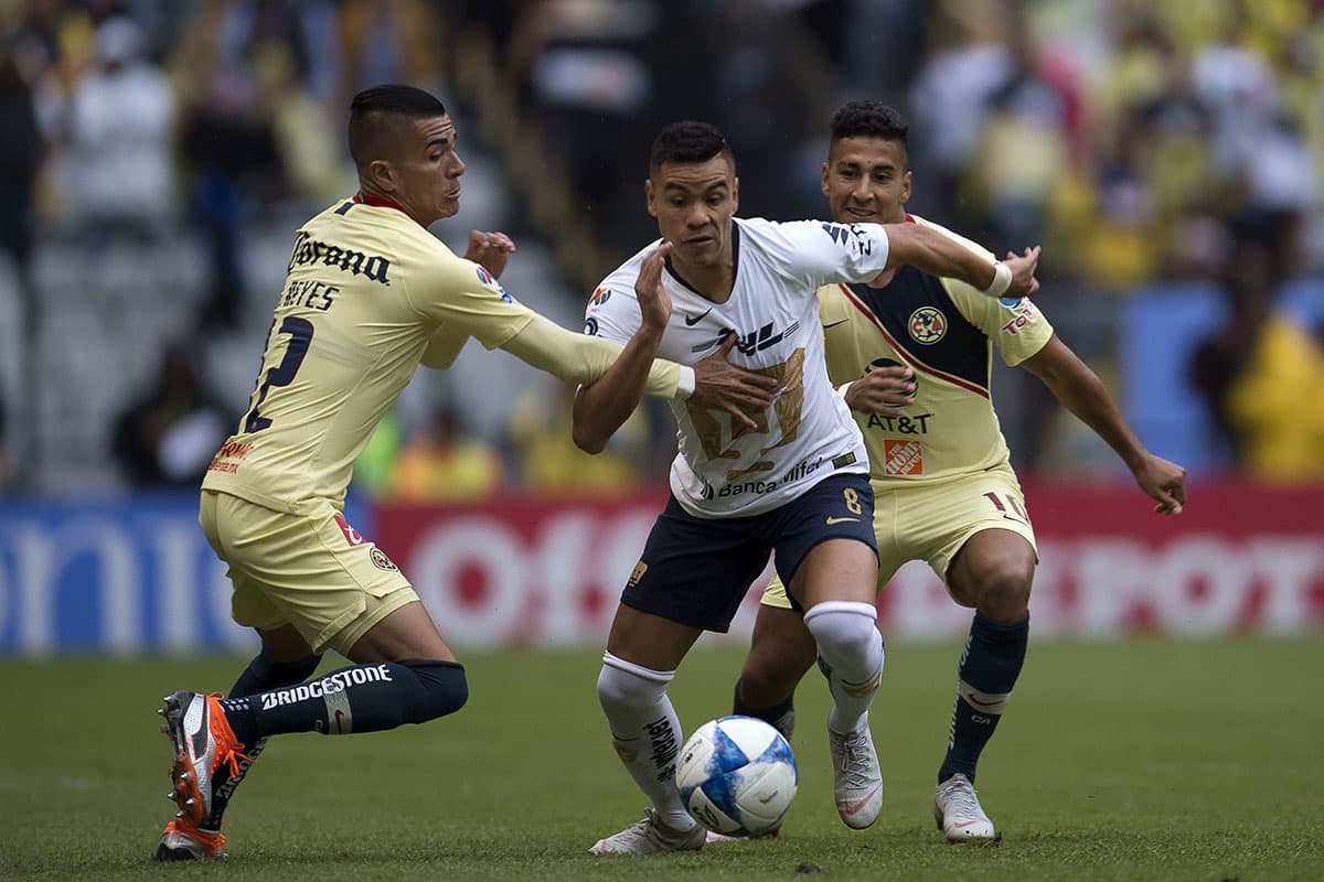 El mediocampista de Pumas, Pablo Barrera (centro) avanza por el medio ante la marca del defensor del América, Paul Aguilar (izquierda).