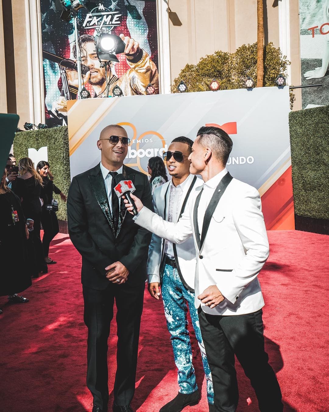 Los boricuas Wisin (i) y Ozuna (c), desfilaron juntos. Wisin, quien está nominado a cinco categorías, optó por el clásico traje negro, mientras que Ozuna (uno de los máximos nominados de la noche con 10 categorías, eligió un pantalón azul con estampado y un saco blanco con solapas negras.