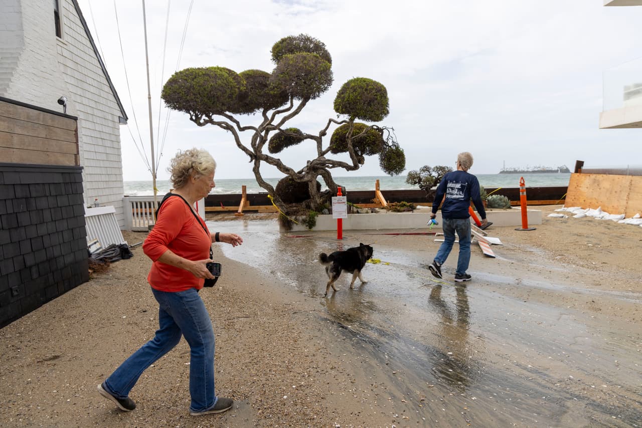 People walk their dog by the boardwalk damaged by Tropical Storm Rachel along Alamitos Peninsula, Sunday, Oct. 11, 2026, in Long Beach, Calif. (AP Photo/Jill Connelly)