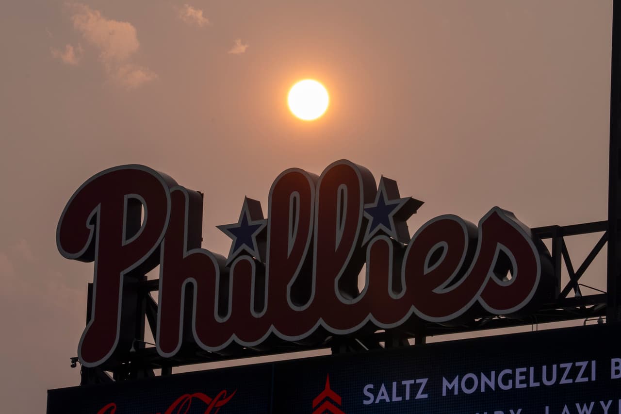 El sol tiene un tono anaranjado debido al humo que desciende de los incendios forestales canadienses mientras se pone cerca del marcador de los Philadelphia Phillies durante la cuarta entrada de un partido de béisbol contra los New York Mets, el jueves 16 de julio de 2026, en Filadelfia.