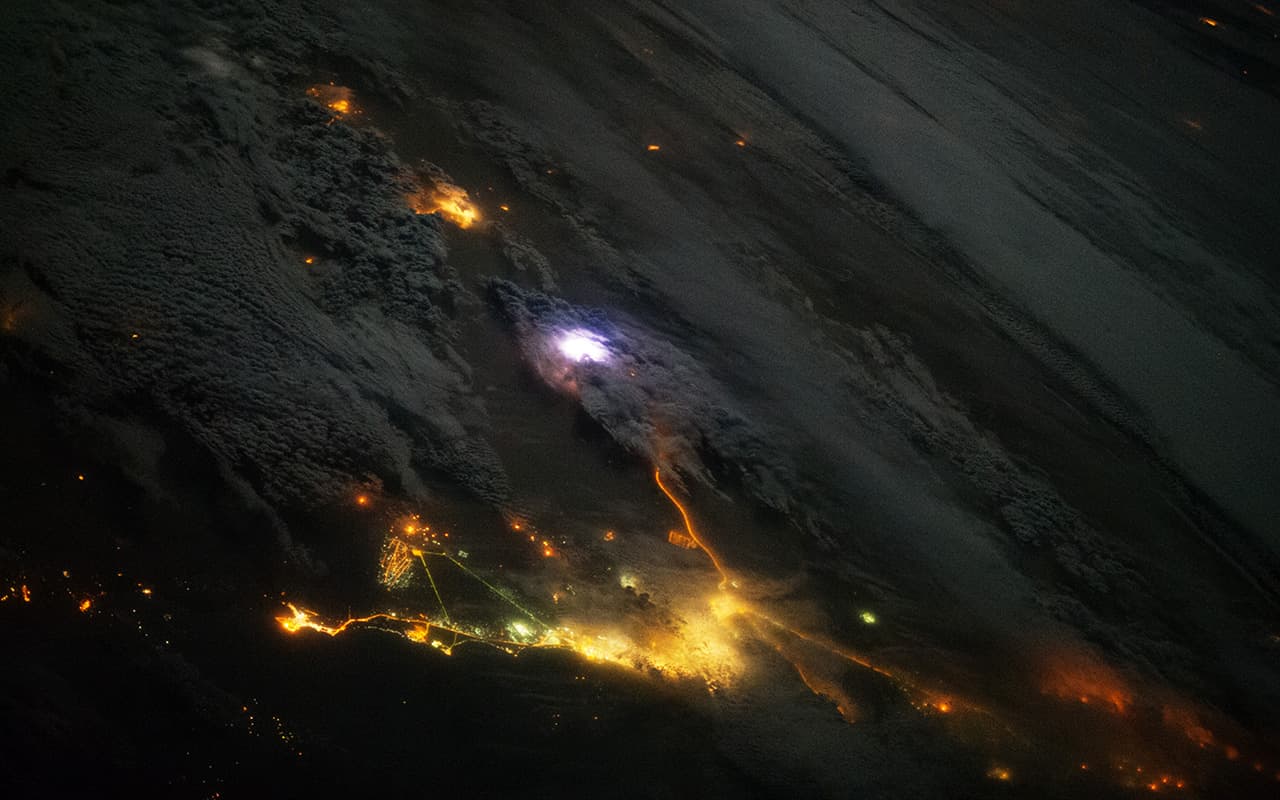 <b>Un rayo desde la estación espacial.</b> Esta foto fue tomada el 12 de diciembre de 2013 muestra un relámpago blanco en medio de las luces amarillas de Kuwait y Arabia Saudita. En la atmósfera de la Tierra, los relámpagos parpadean unas 50 veces por segundo. Los científicos han encontrado evidencia de que los destellos de rayos gamma terrestres pueden ocurrir en la atmósfera con una frecuencia de 500 veces al día. La radiación gamma se asocia con la explosión de estrellas o la fusión nuclear.