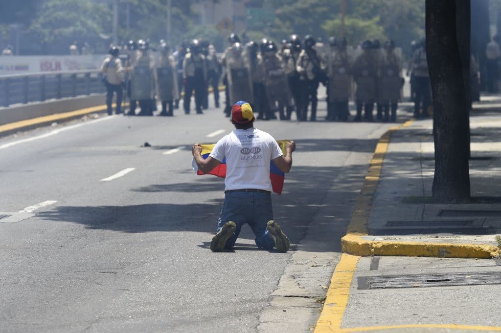 Un manifestante se arrodilla frente a la policía anti-disturbios en una calle de Caracas.