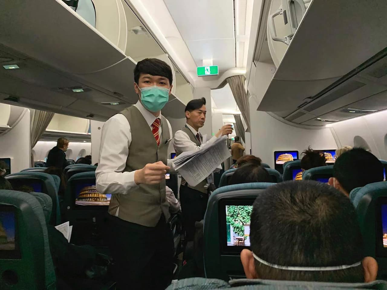 Tripulación de la aerolínea Cathay Pacific entrega planillas con un test de salud a los pasajeros de un vuelo de Hong Kong a Roma.