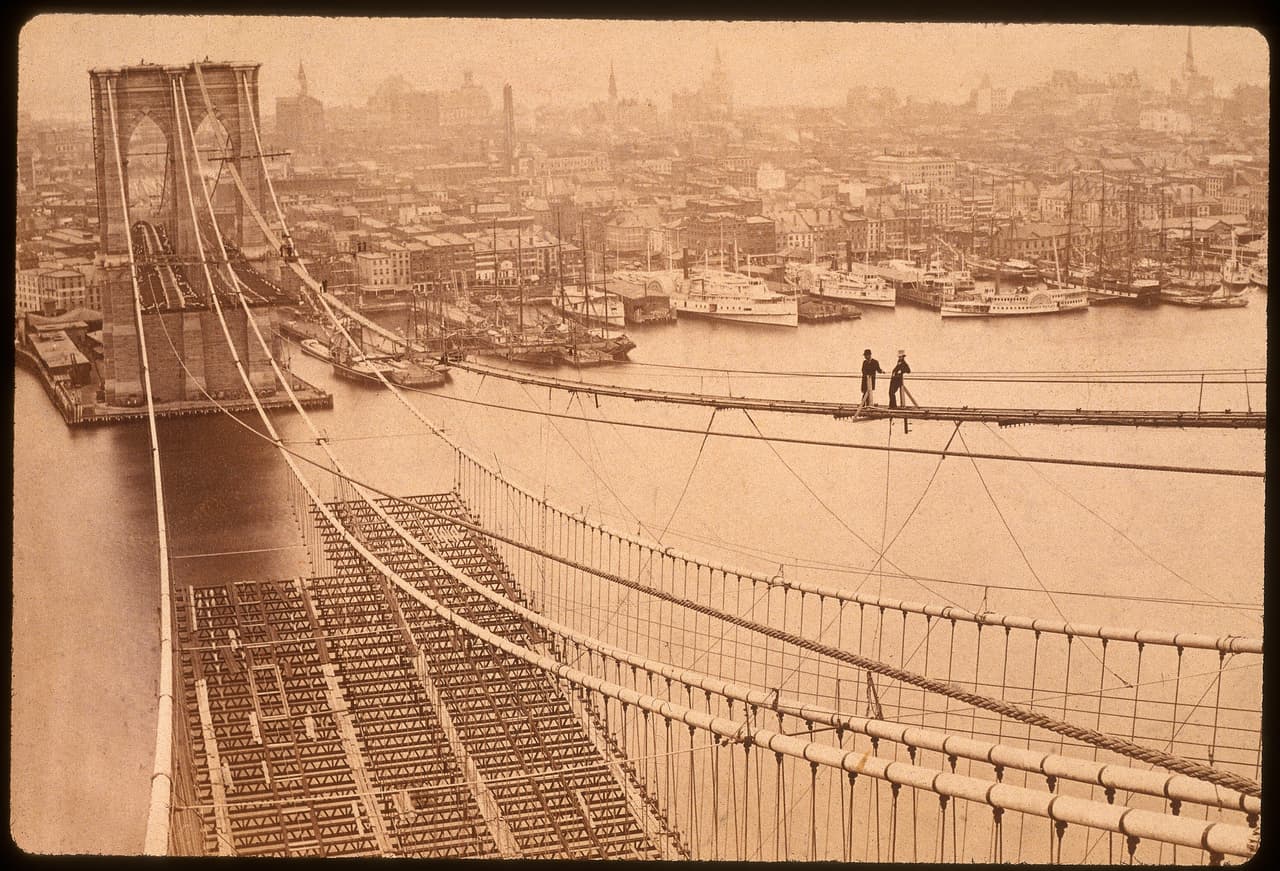 Dos trabajadores en una de las pasarelas de madera que comunicaba los pilares del puente. 27 personas perdieron la vida en accidentes durante la construcción. En la fotografía, tomada en 1877, se puede ver que aún la vía para automóviles no estaba terminada.