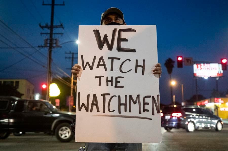 Un manifestante sostiene un cartel que dice 'We Watch the Watchmen' mientras ellos y otros manifestantes se reúnen alrededor de la estación del sheriff del sur de Los Ángeles tras la muerte de Dijon Kizzee en Westmont, South Los Ángeles, California, el 9 de septiembre de 2020. Kizzee fue asesinado por agentes del Sheriff el 31 de agosto después de ser detenido por una violación del código de vehículo mientras montaba en bicicleta.