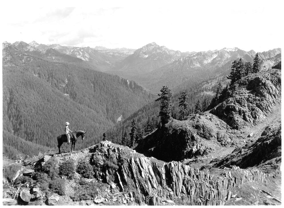 Un visitante al Parque Nacional Olímpico disfruta sobre su caballo la vista del Seattle Creek hacia el Monte Muncaster desde el High Divide.