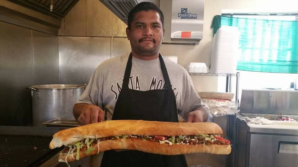 Juan Espinoza carga una enorme torta a la que aún no han bautizado.