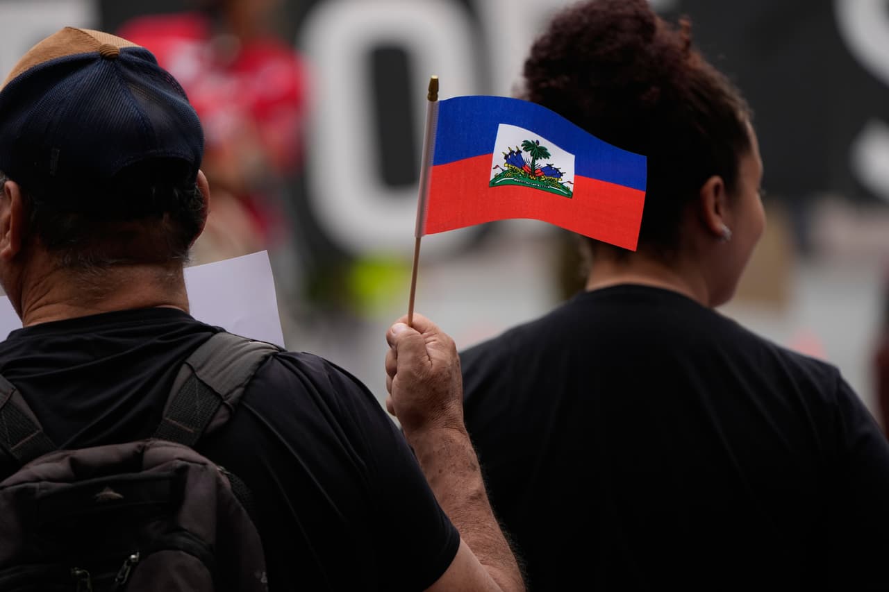 Varias personas portan banderas y pancartas haitianas durante una manifestación en apoyo a los inmigrantes que viven en Estados Unidos con estatus de protección temporal (TPS, por sus siglas en inglés), el jueves 9 de julio de 2026, en San Diego. (Foto AP/Gregory Bull)