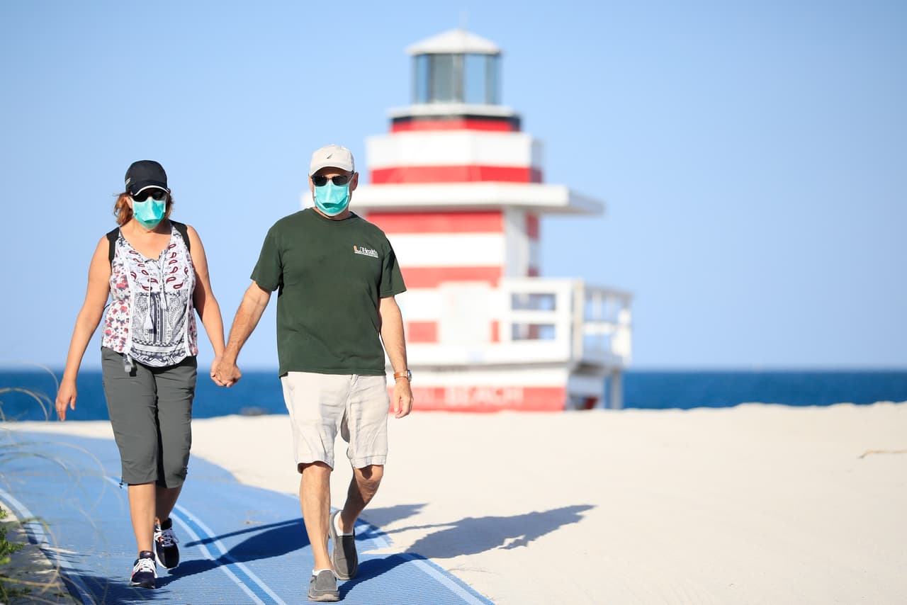 Una pareja camina por las playas de South Beach con tapabocas, tal como es ordenado por el gobierno del condado.