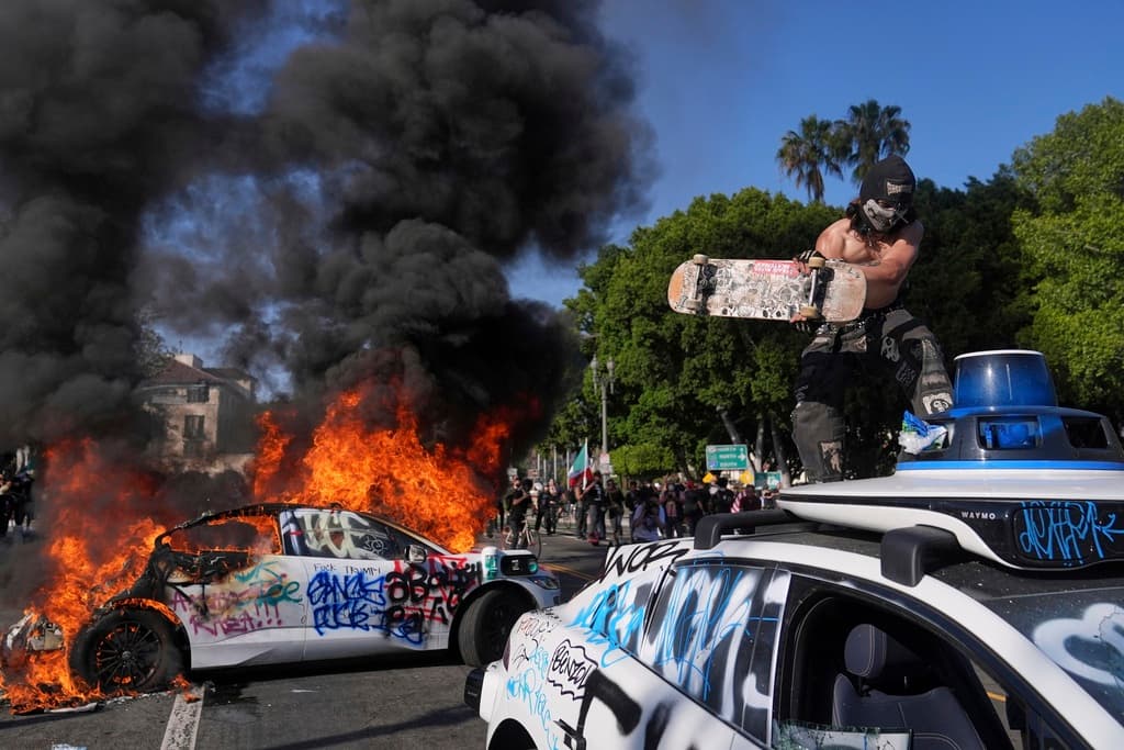 Un vehículo Waymo es vandalizado mientras otro arde cerca de un centro de detención en el centro de Los Ángeles el 8 de junio de 2025.