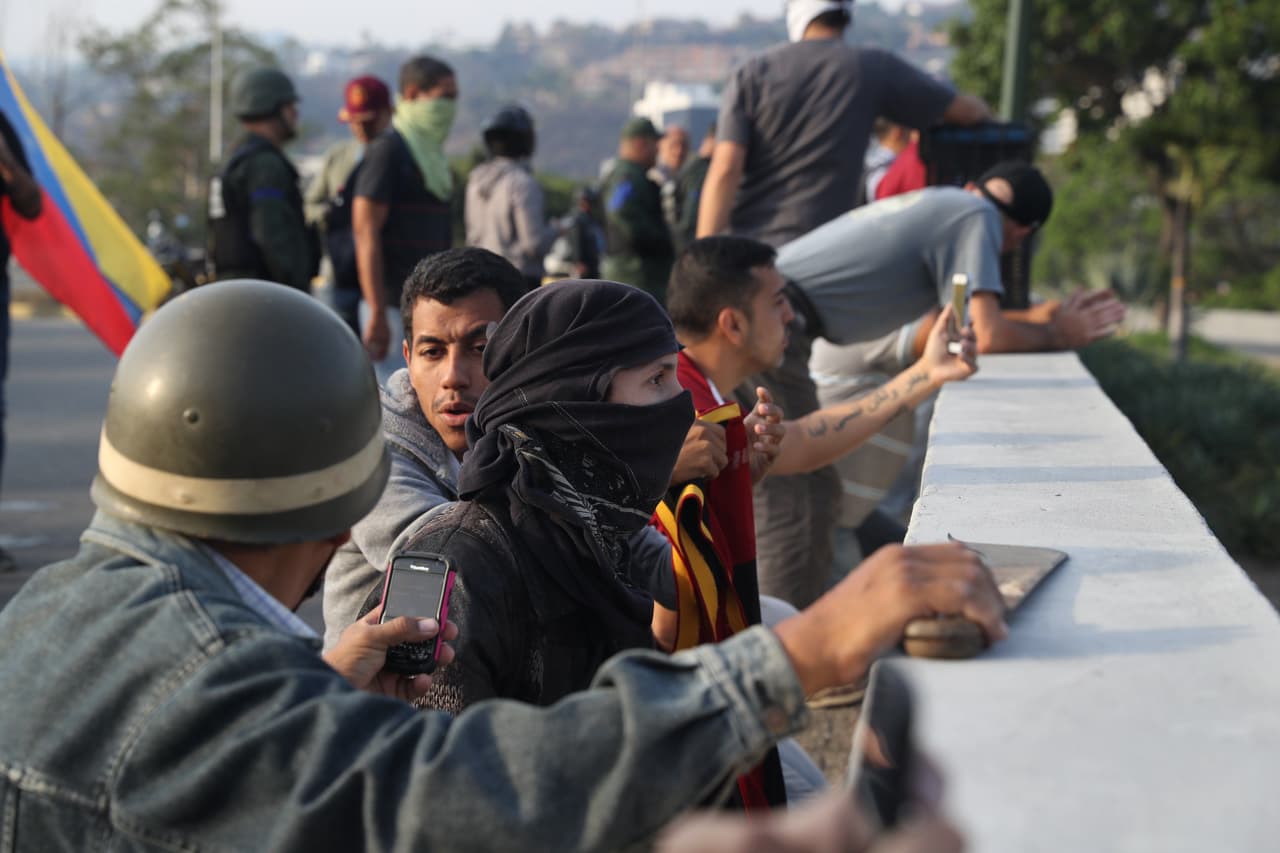 Simpatizantes del presidente interino se protegen de las bombas lacrimógenas que las fuerzas de seguridad leales a Maduro.