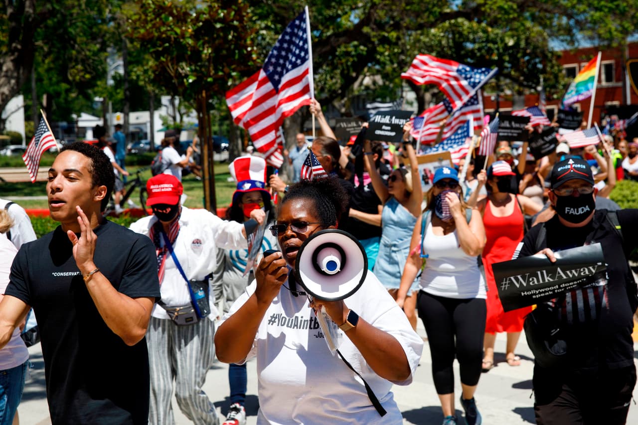 Los manifestantes, algunos de los cuales no usaron la mascarilla facial, ondean banderas mientras marchan en apoyo del presidente de EE. UU. Durante un mitin WalkAway el 8 de agosto de 2020 en Beverly Hills, California.