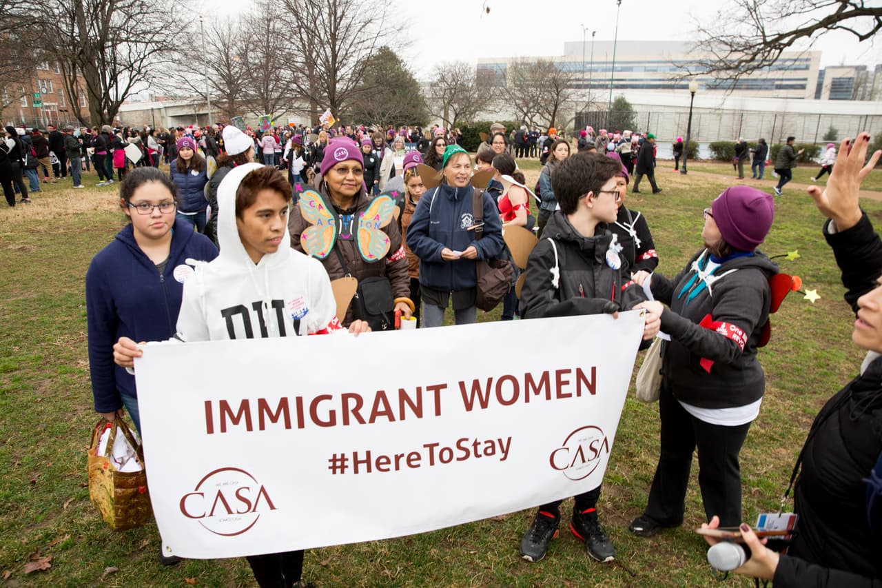 Un grupo de mujeres, muchas mexicanas y centroamericanas, con una pancarta que dice: "estoy aquí para quedarnos".