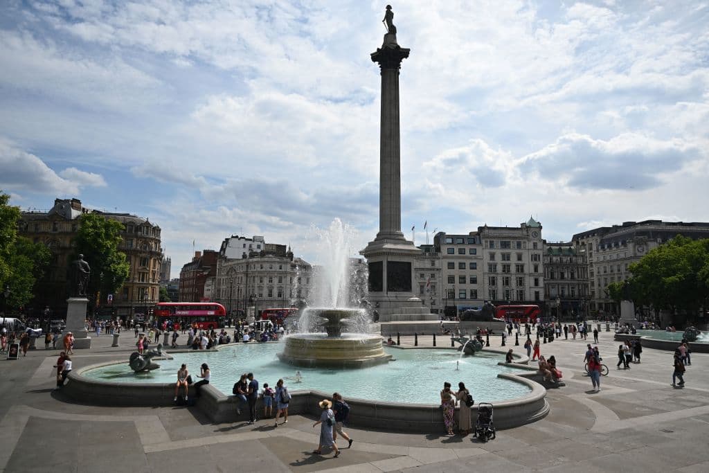 Transeúntes se mojan los pies y se refrescan en la fuente de la céntrica Plaza Trafalgar de Londres.