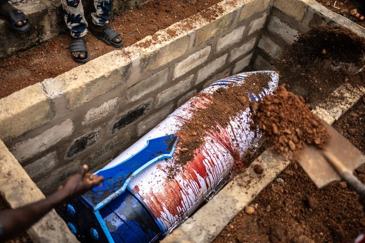 <b>El último adiós termina bajo tierra:</b> Los familiares de Samuel Commey Tetteh arrojan tierra sobre su tumba después de que el ataúd con forma de pluma haya sido bajado al interior. La escena reúne el dolor del entierro con el simbolismo que caracteriza a estas singulares ceremonias.