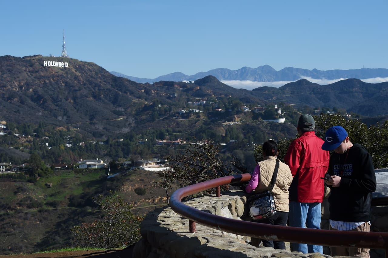 Tourists visiting the Hollywood Bowl Overlook see the Hollywood sign reading "Hollywoed" before repair crews completed their work to return the sign to its normal state, after vandals converted it to read "Hollyweed," January 1, 2017 in Hollywood, California. Police said unidentified thrill-seekers had climbed up and arranged tarps over the two letter "O's" to make them look like "E's," CBS affiliate KCAL reported. Each letter is 45 feet (13.7 meters) high, so the feat would have required not just bravado but considerable athleticism. / AFP / Robyn Beck (Photo credit should read ROBYN BECK/AFP/Getty Images)