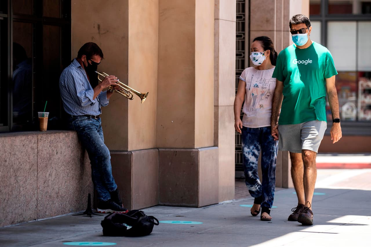 Un músico toca su trompeta en una calle de Pasadena, California, al paso de dos jóvenes que cubren su rostro con una mascarilla. El gobernador de California dio la orden de cerrar otra vez algunos negocios, a causa del incremento alarmante de nuevos casos de coronavirus.