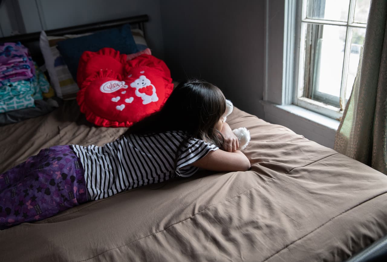Una pequeña de 8 años, solicitante de asilo, mira por la ventana de su habitación durante el aislamiento. La niña cursa el tercer grado y como millones en el país, no ha asistido a las instalaciones de la escuela desde hace varias semanas. La familia no tiene servicio de internet en casa y la pequeña no ha podido participar las clases en línea junto a sus compañeros.