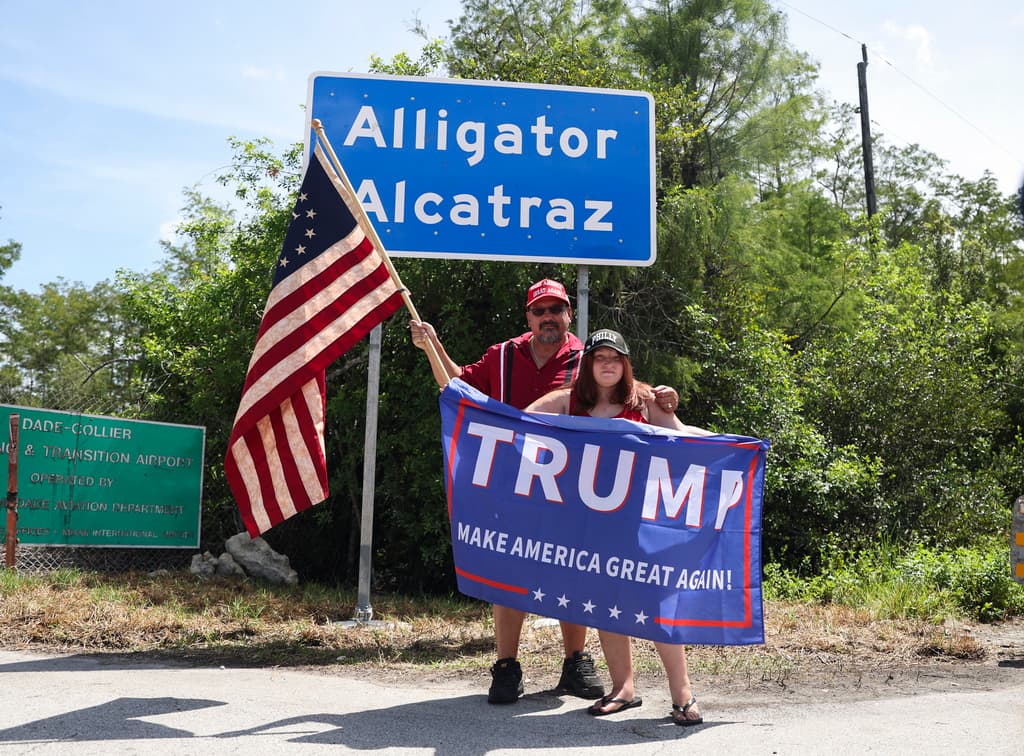 David Mourer y Rana Mourer posan para una foto frente a un cartel que dice Alcatraz de los Caimanes a las afueras del Centro de Entrenamiento y Transición Dade-Collier. Funcionarios estatales de Florida y seguidores de las políticas migratorias del expresidente Donald Trump defienden el centro como una
<b>medida efectiva para disuadir la inmigración irregular</b>, asegurando que cumple con todos los estándares legales de detención.