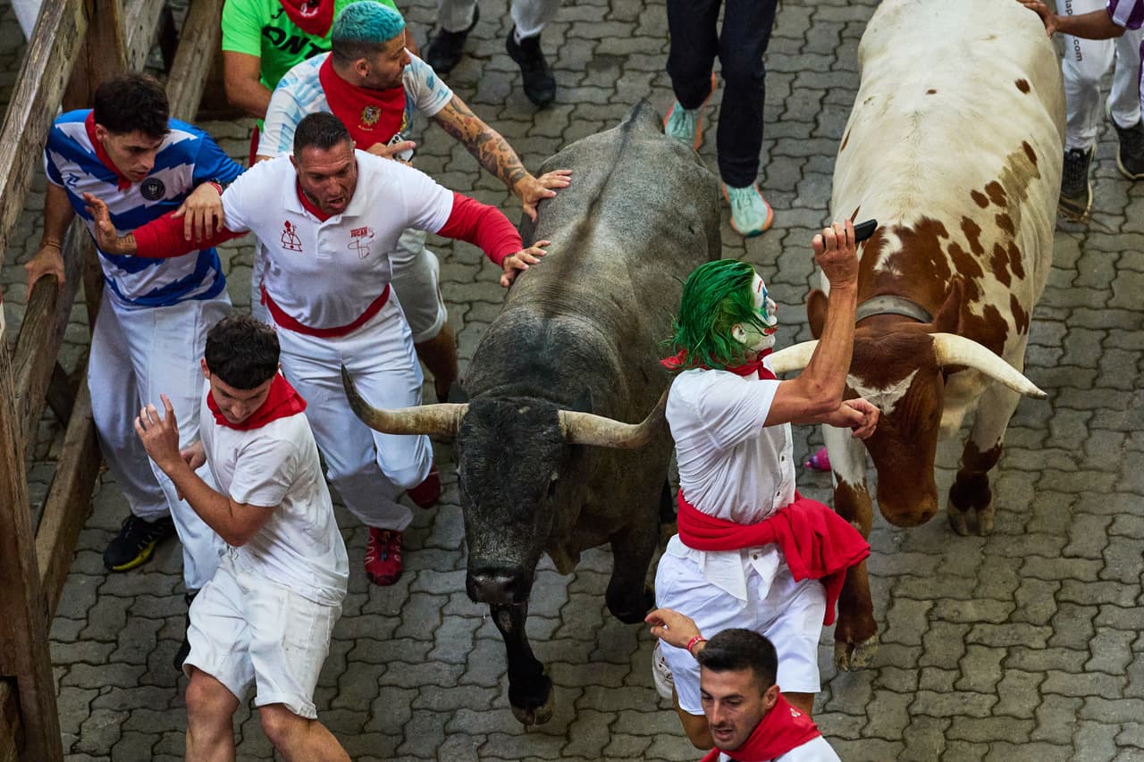 Las personas tratan de esquivar a los toros mientras corren, al igual que una persona pintada del Joker trata de tomar una foto mientra es alcanzado por uno