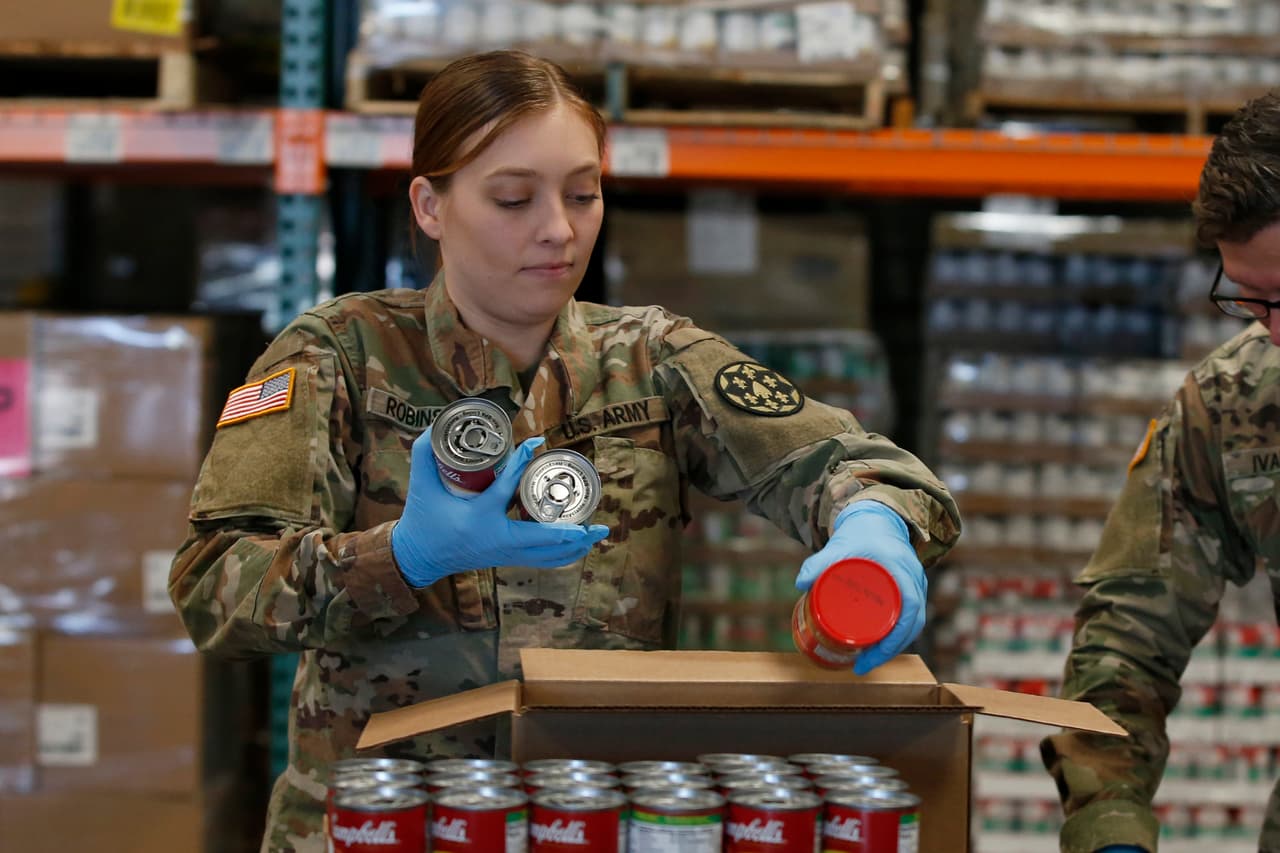 Los bancos de comida han visto una reducción en el número de voluntarios debido a la orden estatal de quedar en casa para frenar la propagación del coronavirus. Kansae Robinson, de la Guardia Nacional de California, organiza comida enlatada y en frascos en una caja de suministros en el Banco de Comida de Sacramento. (AP Photo/Rich Pedroncelli)